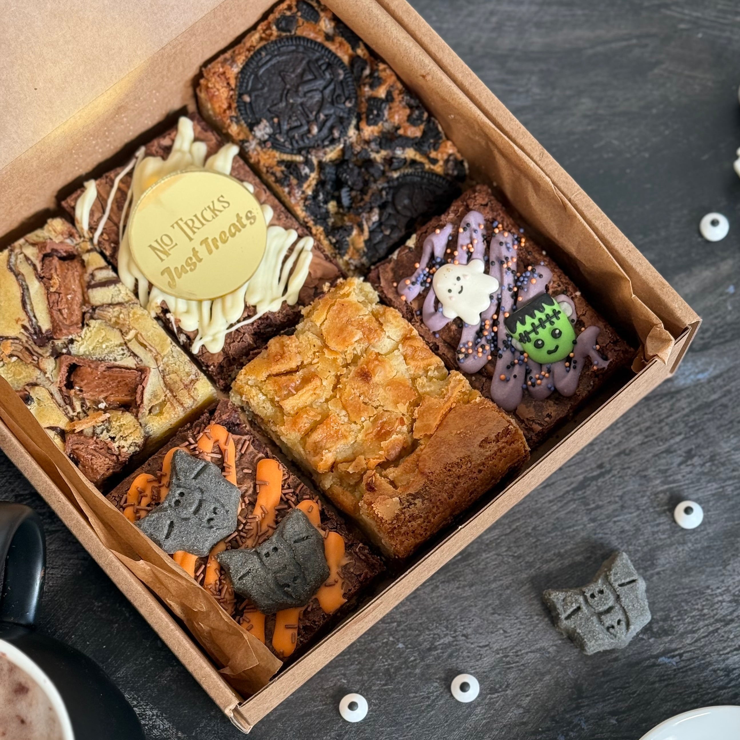 Box of Halloween-themed brownies with decorative elements on a dark surface.