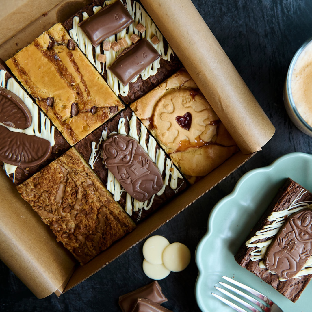Cheshire Bakes mixed brownie box topped with chocolate bars, white chocolate drizzle, and fudgy brownie slices served on plates – handmade brownies delivered across the UK.
